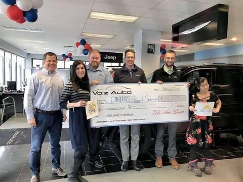 Group holding a large donation check inside an auto showroom.