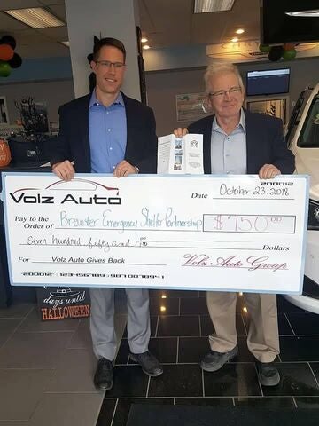 Two men holding a donation check inside a dealership.