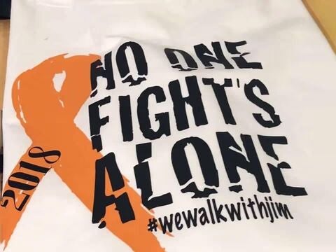 Shirt with an orange ribbon and the phrase “No One Fights Alone.”