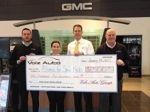 Group holding a large donation check inside a GMC dealership.