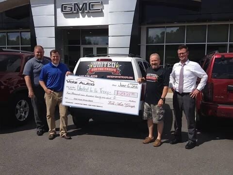 People posing with a donation check outside a GMC dealership.