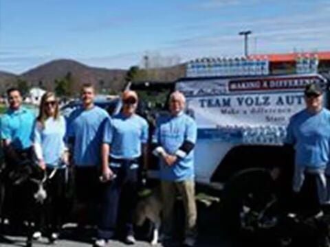 Group in blue shirts standing with a Team Volz Auto truck.