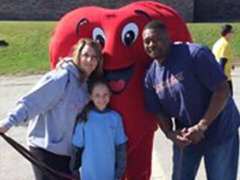 People posing with a large heart mascot outdoors.