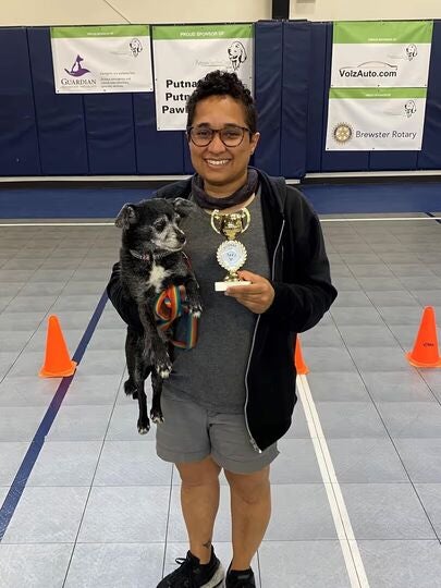 Person holding a small dog and a trophy inside a gym.