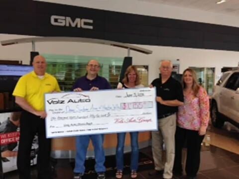 Group holding a large donation check inside a GMC dealership.