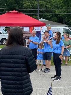 Group in blue shirts speaking at an outdoor event.