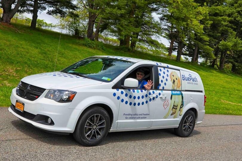 White 'BluePath Service Dogs' van with a man waving from window