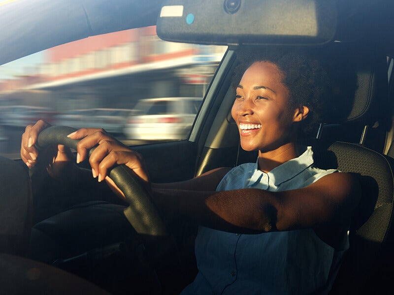 Happy woman driving, smiling brightly as sunlight highlights her face.